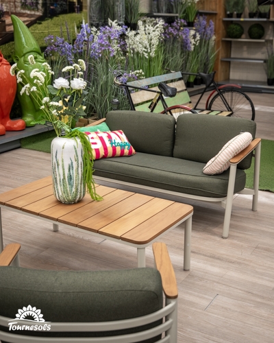 Salon de jardin avec canapé 2 places, fauteuil et table basse en métal blanc et bois, coussins verts, dans un magasin.